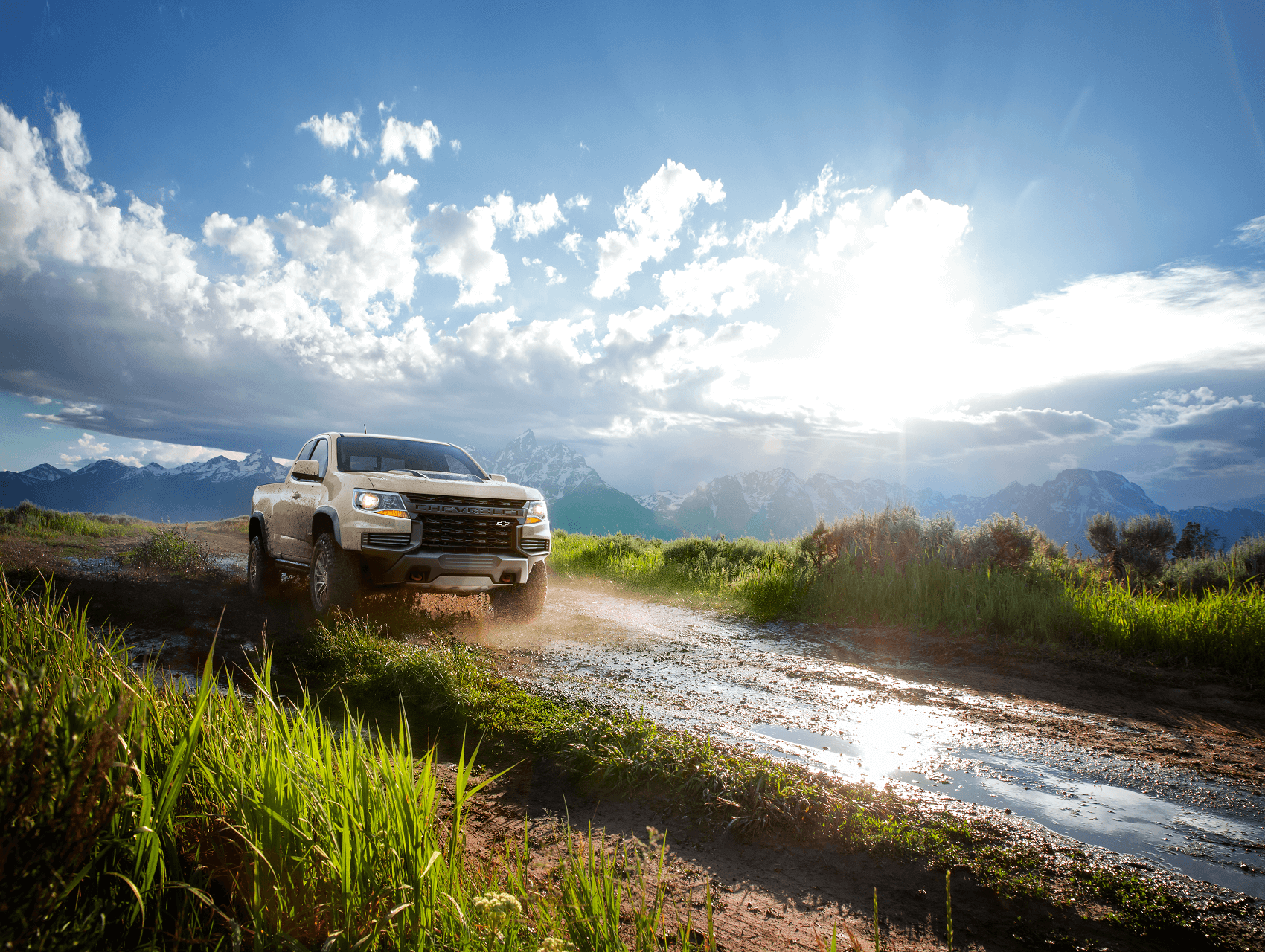Chevrolet Colorado driving on a dirt road with mountain and bright blue sky background